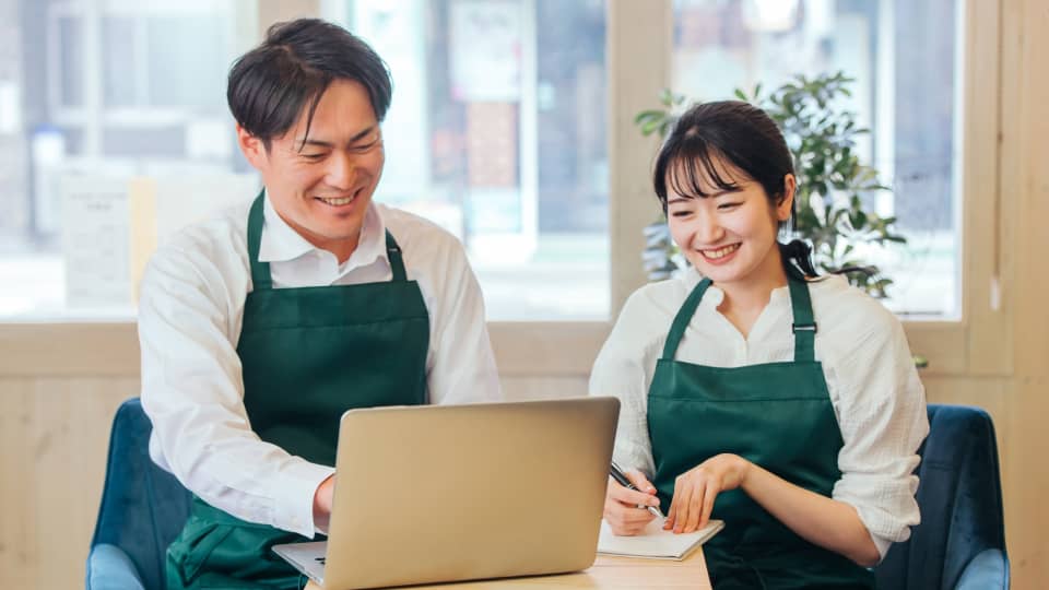 パソコンを見ながら打ち合わせをするカフェ店員の男女
