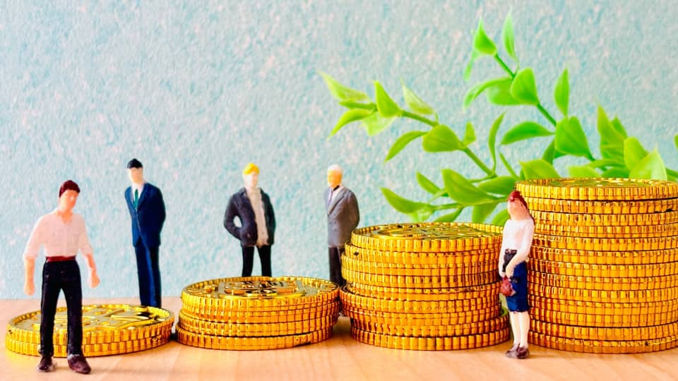金貨の山の上に立つ人物フィギュアと異なる高さが示す経済格差のイメージ